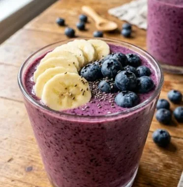A vibrant blueberry banana smoothie in a glass with fresh blueberries and banana slices