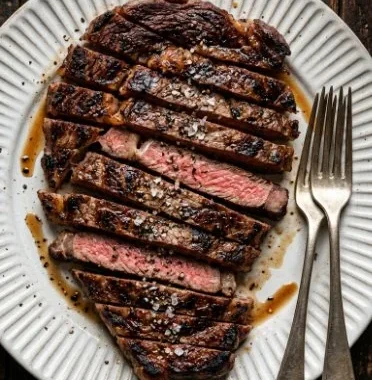 Juicy Coffee Rubbed Steak garnished and ready to serve on a wooden cutting board.