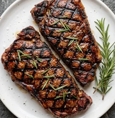 Grilled New York Strip Steak on a plate with herbs and sides