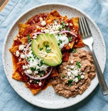 Red Chilaquiles 2 Plate of vibrant Red Chilaquiles topped with cilantro and cheese.
