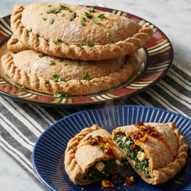 Chili crisp spinach and feta hand pies on a patterned plate, with one cut open on a blue plate showing spinach, feta, and chili crisp filling